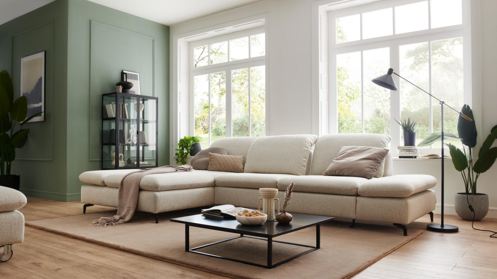 Grosszügiges Wohnzimmer mit hellbeiger Eckcouch, schwarzem Couchtisch und viel Tageslicht durch grosse Fenster. plaintext Kopieren Bearbeiten